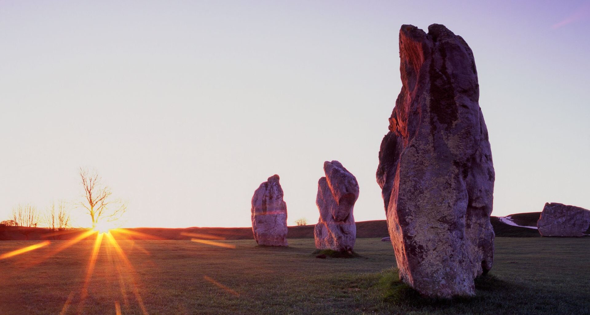 A series of stone pillars are seen in the setting sun overlooking a field