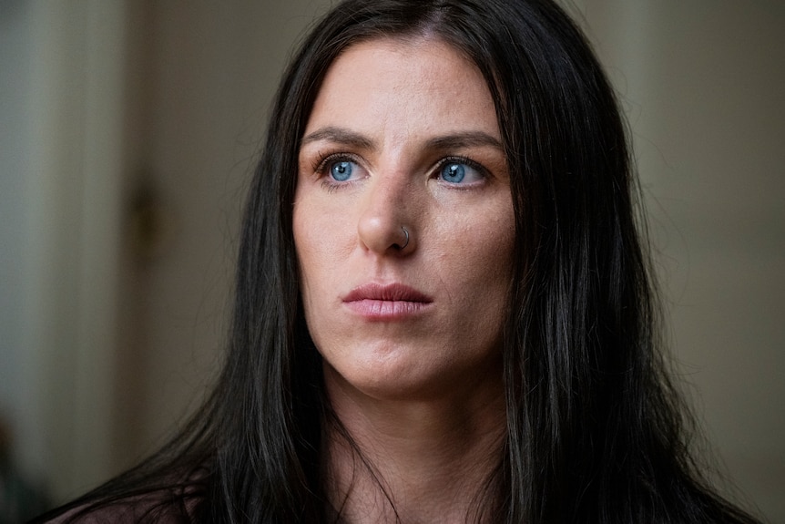 A woman with long dark hair looks off to the side of the camera.