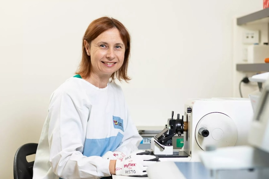 A woman in a lab coat sits with a microscope.