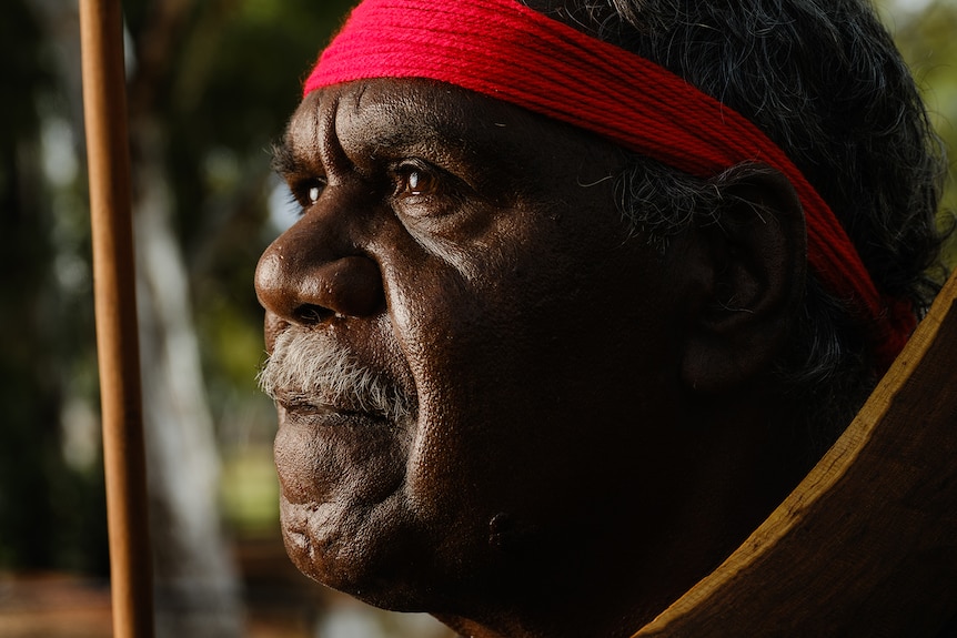 A man with a red tie around his head, looking into the distance with shadow covering the side of his face.