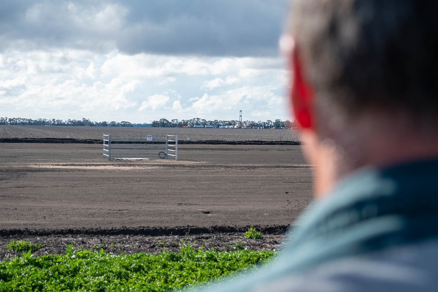 A photo over a farmer's shoulder of a drill rig operating in the distance near Dalby, June 2021.