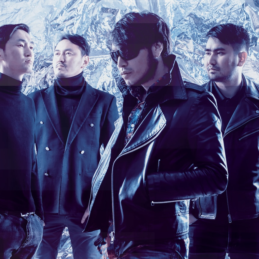 Four members of Mongolian band The Lemons wearing dark jackets standing in front of a shiny, crinkled foil backdrop