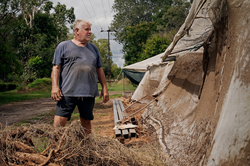 A man stands next to a fence covered in mud.