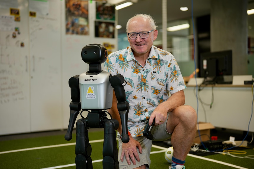 Toby wears a colourful shirt and kneels near a robot.