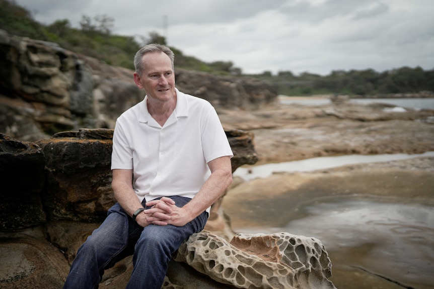 A man sits on a rock near the ocean