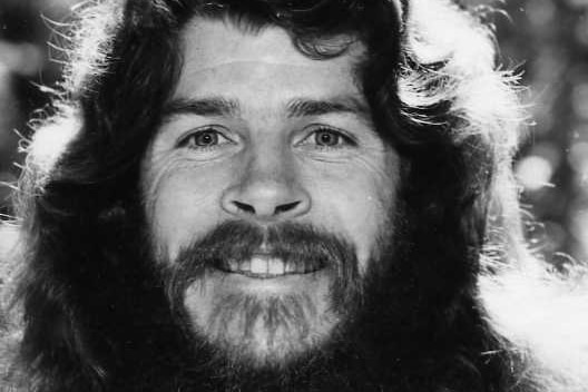 old phot of a man with long hair and mustache smiling into the camera