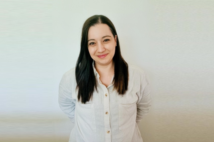 A woman in her mid-30s smiling to the camera on a plain background.