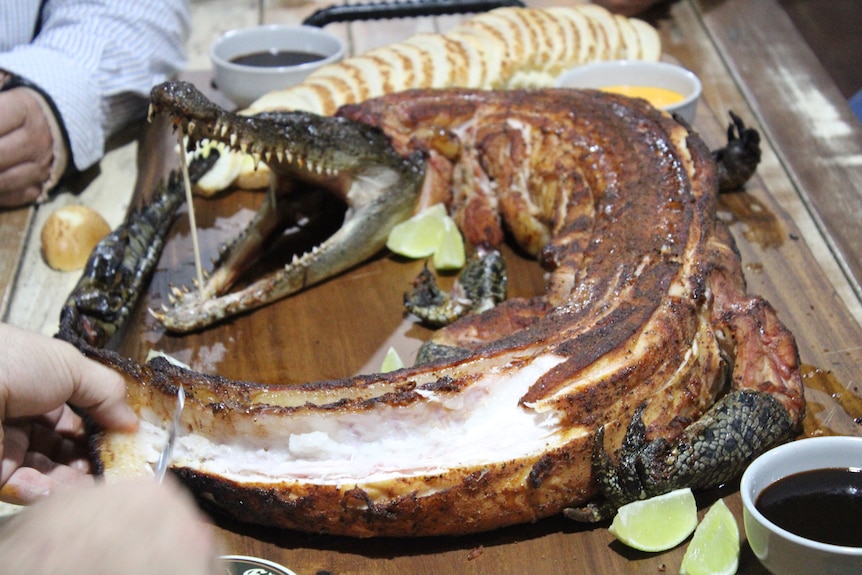 A whole smoked crocodiles being carved into for eating.