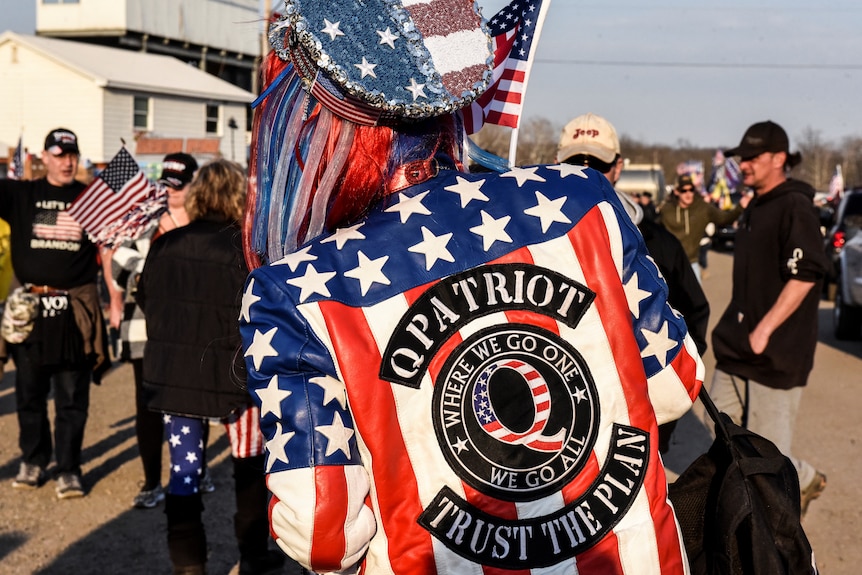 A woman wears a jacket with the QAnon logo that says "trust the plan". 