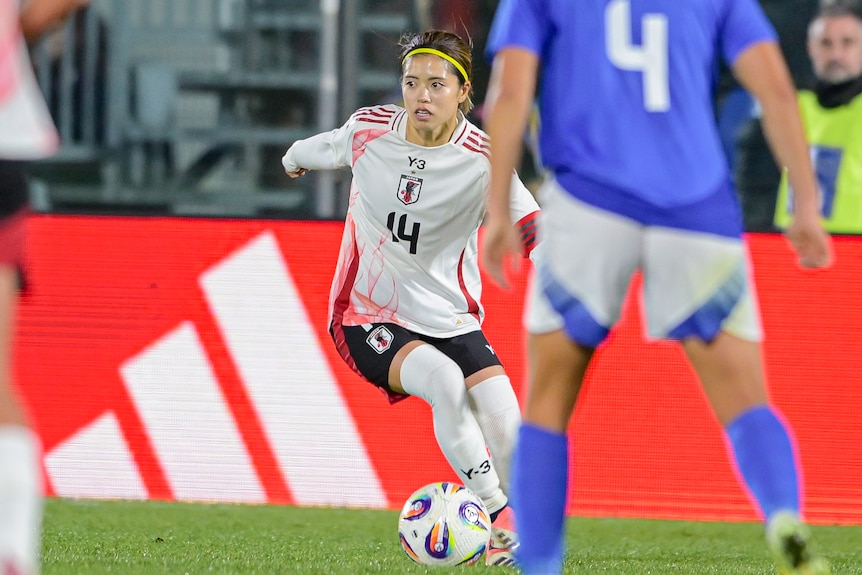 Yui Hasegawa kicks a soccer ball around an opponent and looks to the side.