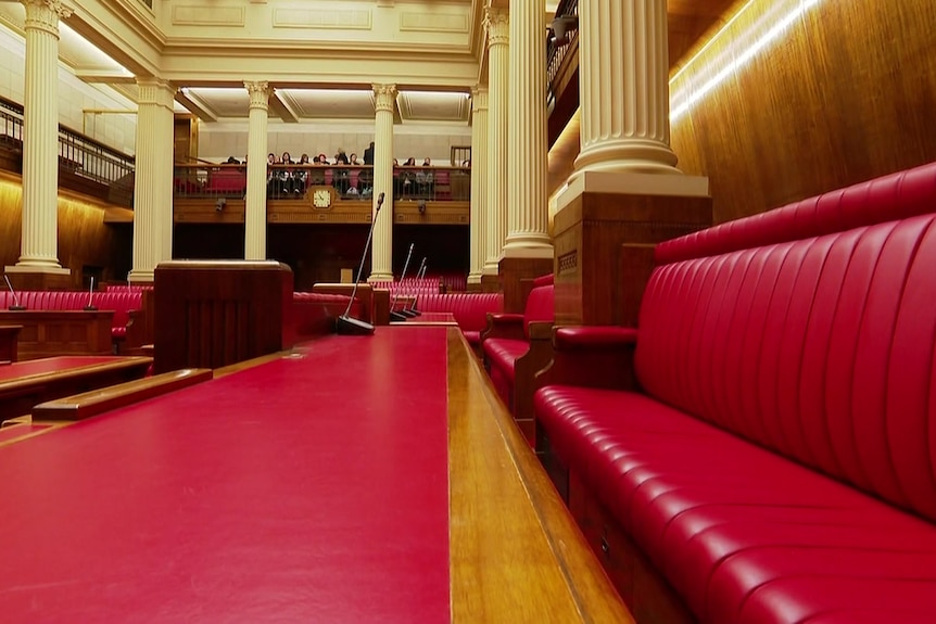 A red desk and red leather seats in a parliamentary chamber