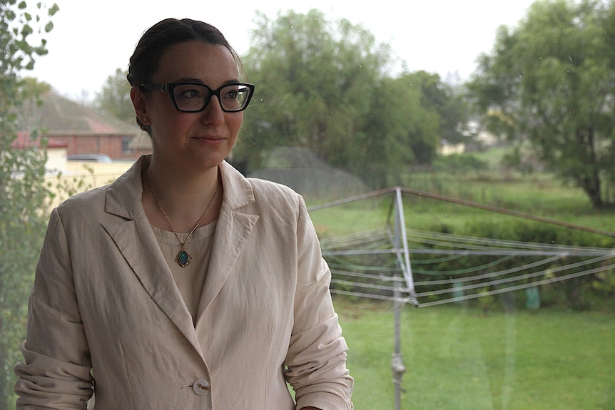 A dark-haired woman in glasses smiles while standing in a backyard with a clothes hoist.