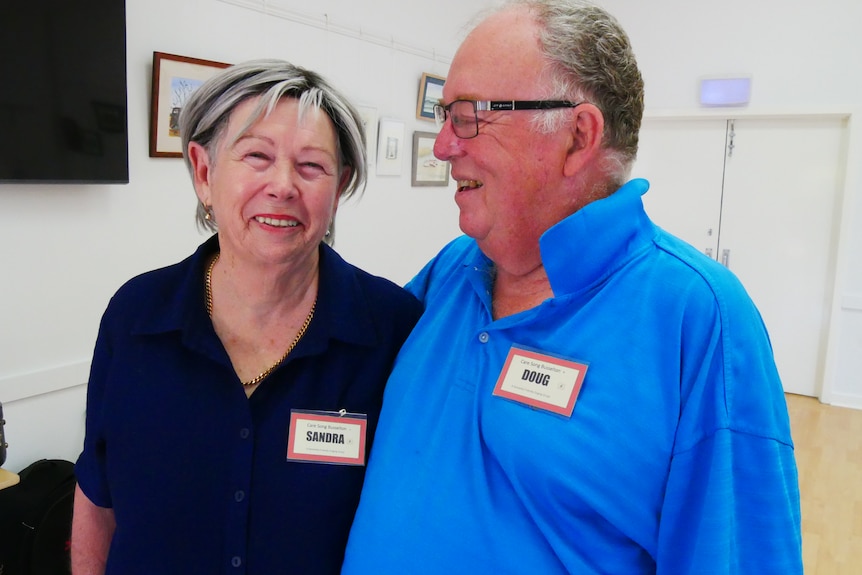 An older woman and an older man laugh together while standing in a communal space.