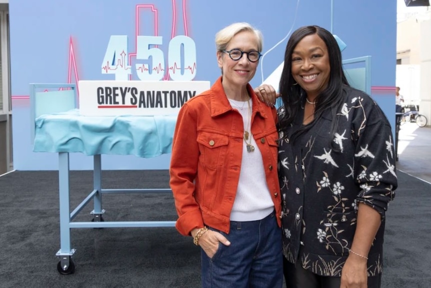 Two women standing in front of a large cake.