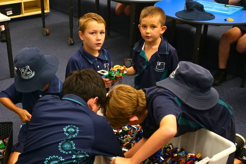 Five children wearing blue school uniforms gathered around a tub of Lego.