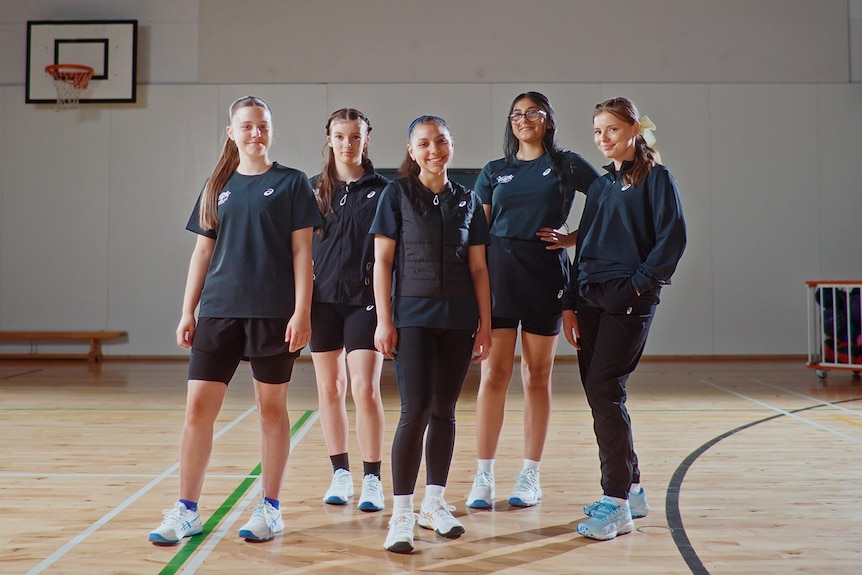 Group of women wearing dark activewear stand on basketball court.