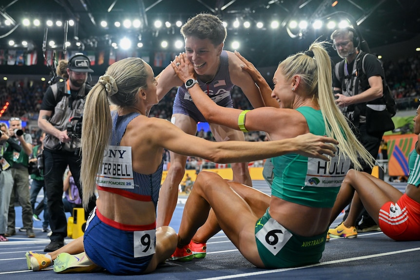 Nikki Hiltz (standing) hugs Georgia Hunter Bell and Jess Hull (sitting) after the 1,500m at the world indoor championships.