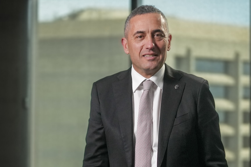 A man stands in an office with buildings outside of the window