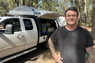 Man in place shirt smiling at camera with car and boat on roof 