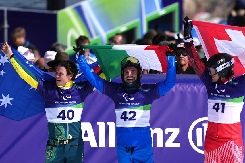Three para-snowboarders raise the national flags of their country aloft after winning Paralympic medals