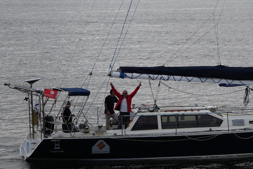 A man raises his arms in triumph on a boat