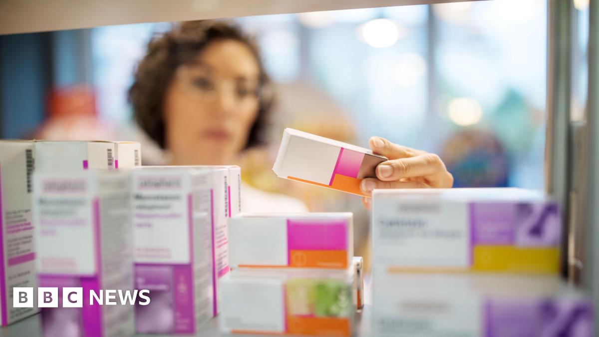 A woman, not in focus, handles different packets of tablets in a pharmacy setting