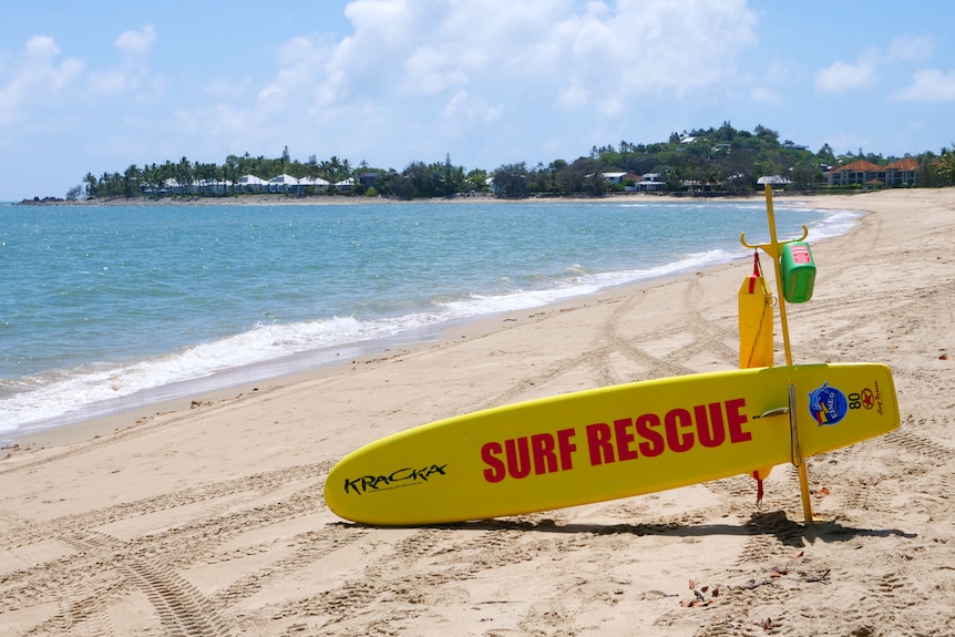 A surf rescue board is lying on its side on the sand at a tropical beach.