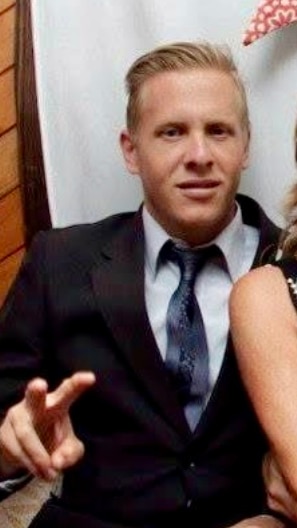 A man wears a suit and signs a peace symbol with his hand.