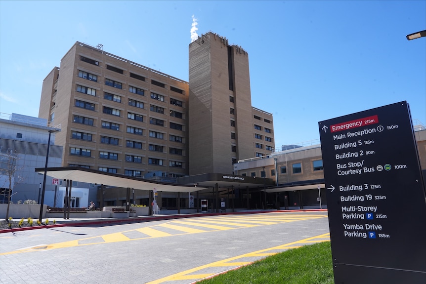A nine-storey brick hospital building with a car turning circle out the front.