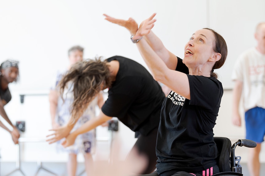 Woman in wheelchair moves her arms while others follow her example