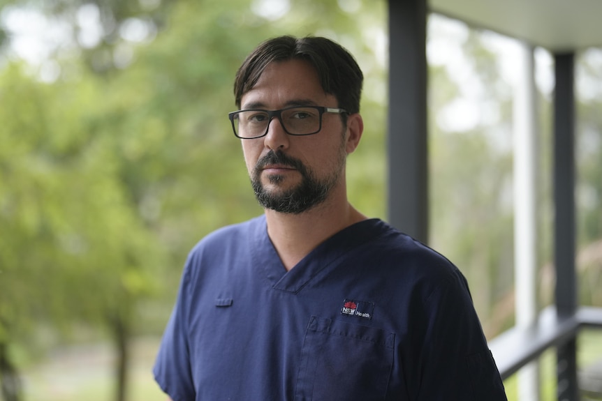 A man in navy nurse's uniform standing next to a sign for Cumberland Hospital.