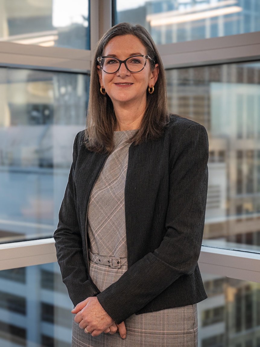 Clare Savage stands by an office window, overlooking other office towers