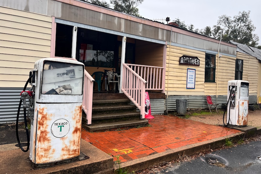 The exterior of a weathered regional general store with two dilapidated petrol pumps out the front.