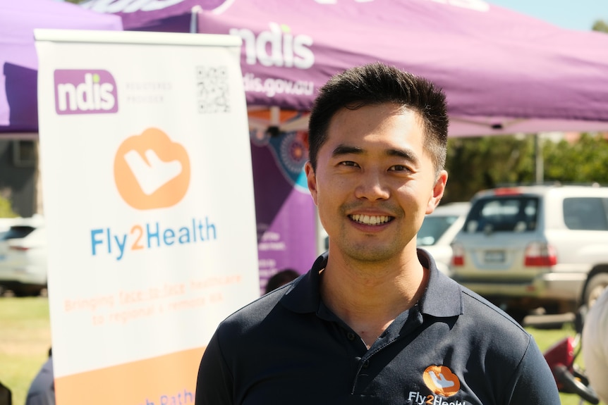 Image of Kennedy Lay smiles at the camera behind a Fly2Health sign.