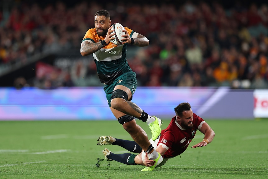 Rugby player skips out of a tackle, holding football in both hands