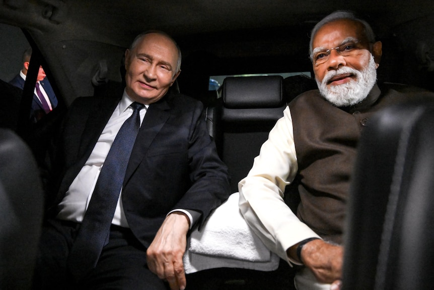 Two men sit smiling in the back of a car with black leather seats