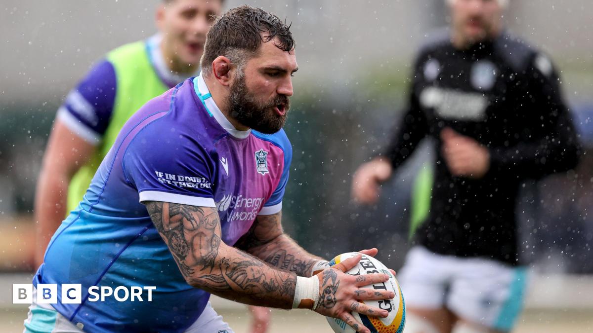 Jamie Bhatti in the purple shirt of Glasgow Warriors holds the ball during a warm-up, with two team-mates indistinct in the background.