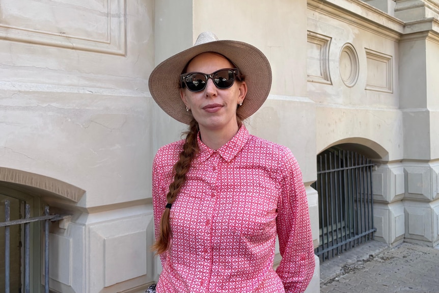 A woman in a hat stands outside a historic building