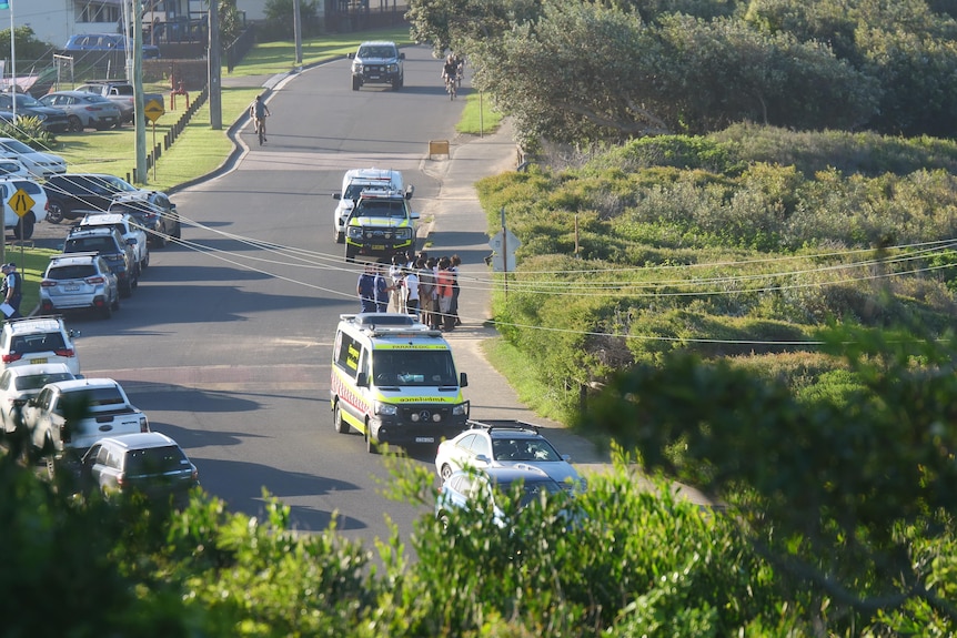 A group of people speaking to an ambulance worker, on a residential street.