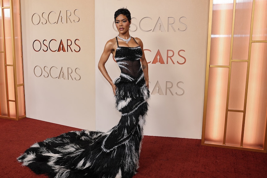 A black woman with short hair in a black dress streaked with white, with a long train.