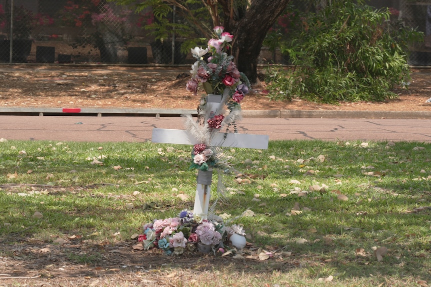 A cross with flowers, planted on a grassy patch near the road.