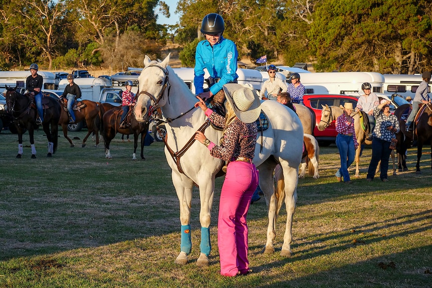 A woman wearing bright pink jeans speaks to a woman riding a horse.