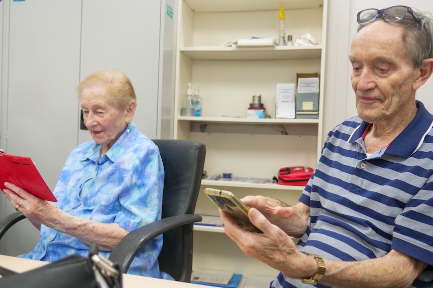 an elderly man and woman using their mobile phones sitting down