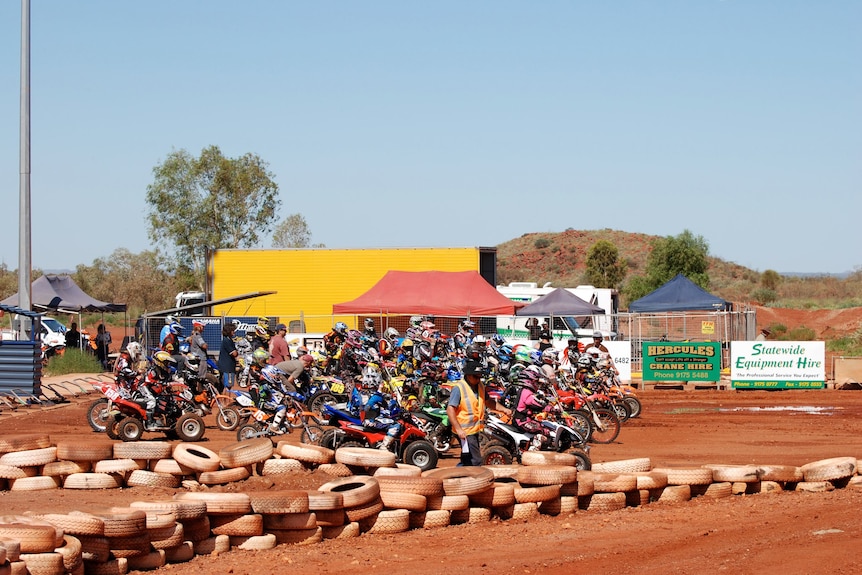 A long line on young-looking motocross riders line the starting line of a race.