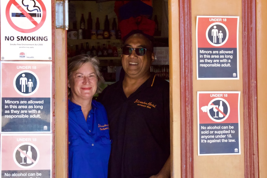 A man and woman stand in a pub doorway.
