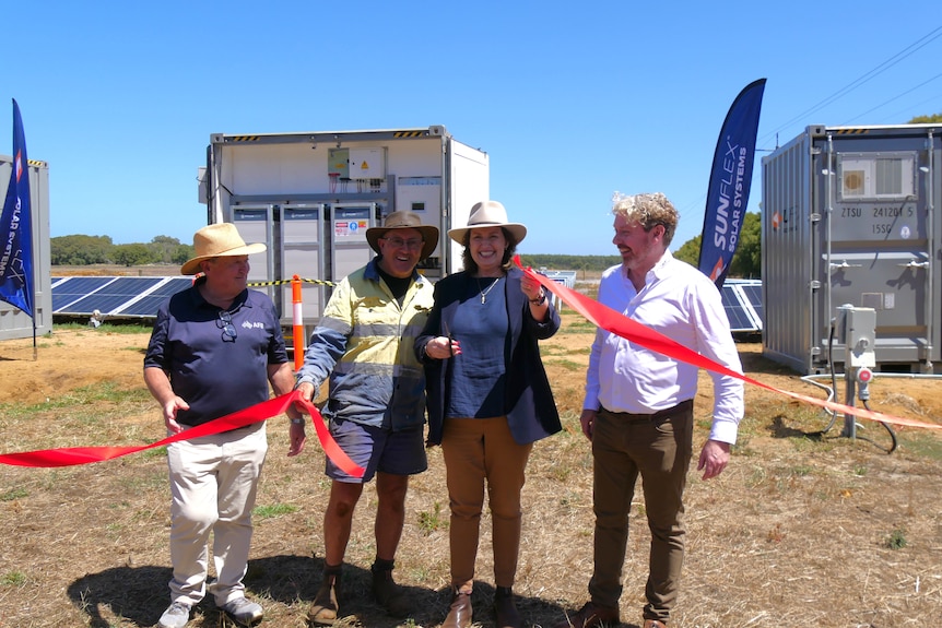 Four people standing behind red cut ribbon smile at camera.