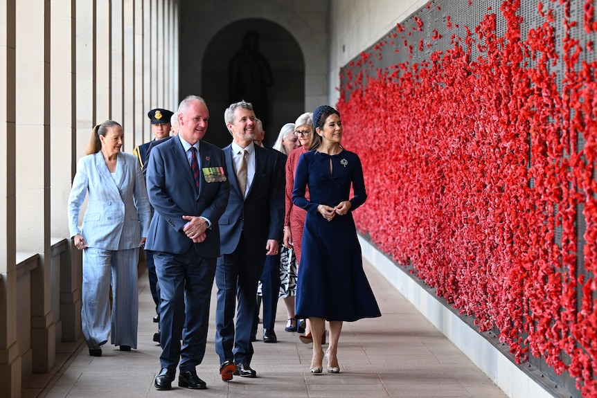 A man and woman walk by a war memorial wall.