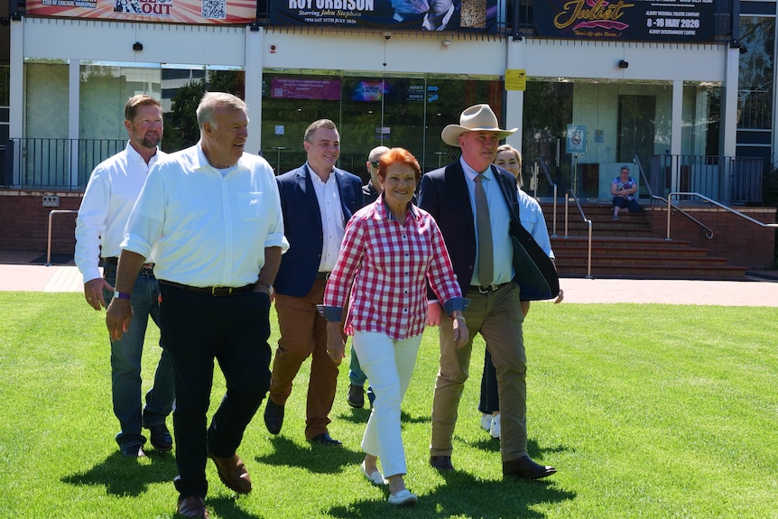 One Nation leaders david farley, pauline hanson and barnaby joyce walk alongthe grass