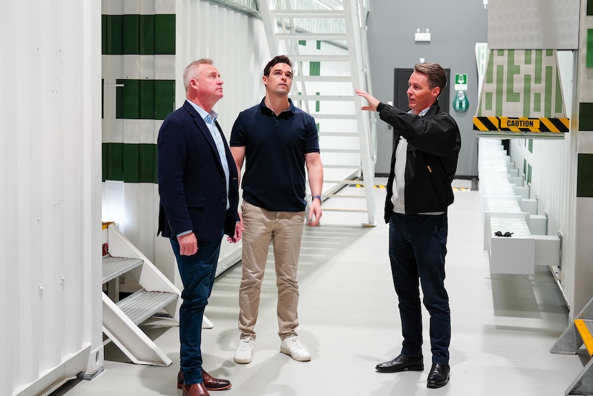 Three men in a white building, gesturing.