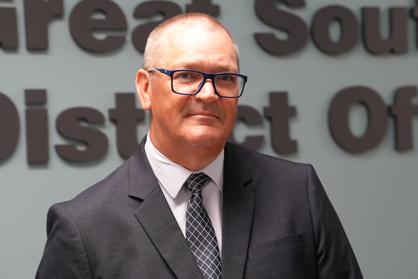 A bald man wearing a suit and glasses looking serious at the camera.